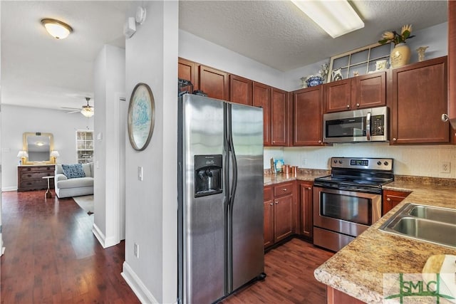 kitchen with a sink, stainless steel appliances, baseboards, a ceiling fan, and dark wood-style floors