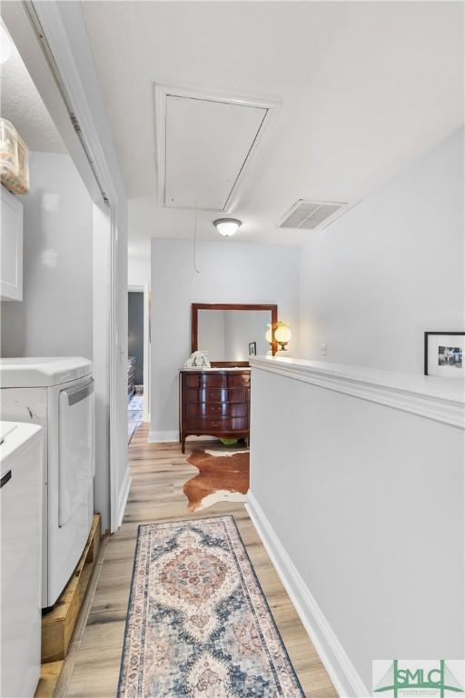 corridor with light wood finished floors, attic access, baseboards, visible vents, and washing machine and dryer