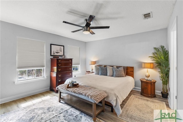 bedroom with a ceiling fan, baseboards, visible vents, and wood finished floors