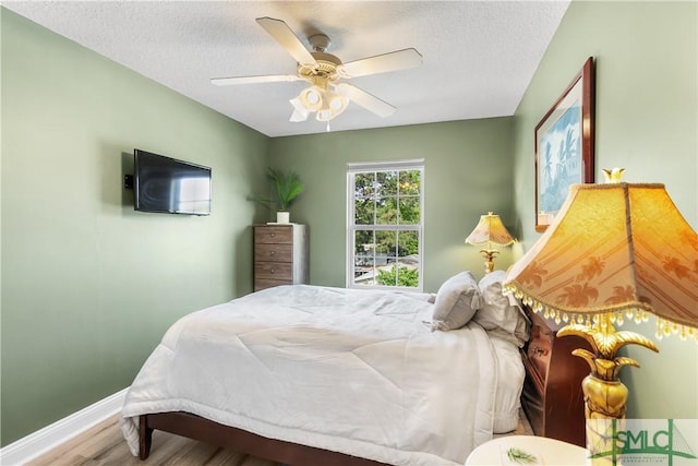 bedroom featuring baseboards, a ceiling fan, a textured ceiling, and wood finished floors