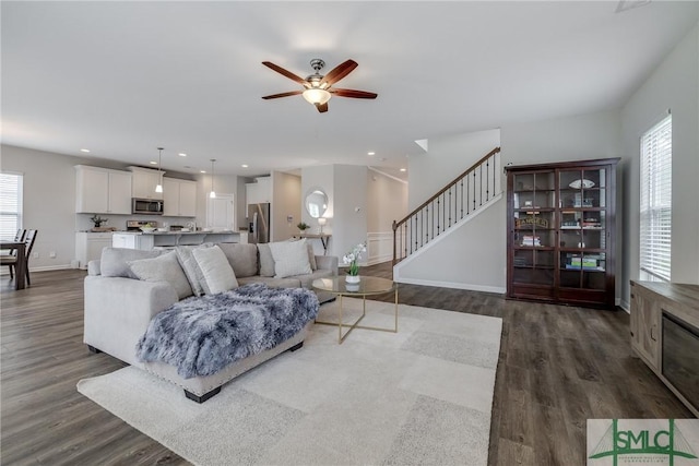 living room with stairway, a ceiling fan, and dark wood-style flooring