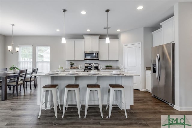 kitchen with dark wood-style flooring, appliances with stainless steel finishes, white cabinets, and a kitchen bar