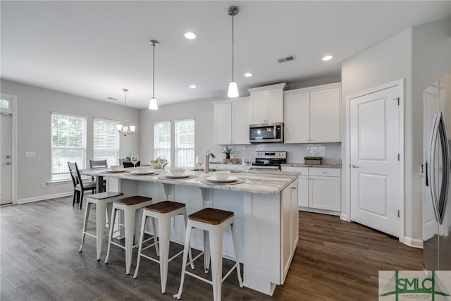 kitchen featuring white cabinets, dark wood-style flooring, appliances with stainless steel finishes, a kitchen breakfast bar, and visible vents