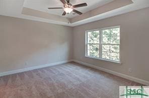 empty room featuring baseboards, carpet flooring, ceiling fan, and a tray ceiling