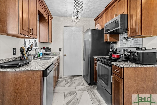 kitchen with decorative backsplash, brown cabinetry, a textured ceiling, a sink, and stainless steel appliances