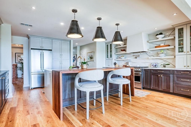 16 Modena Island Dr, Savannah, GA 31411 - kitchen with premium appliances, open shelves, custom range hood, an island with sink, and light wood finished floors