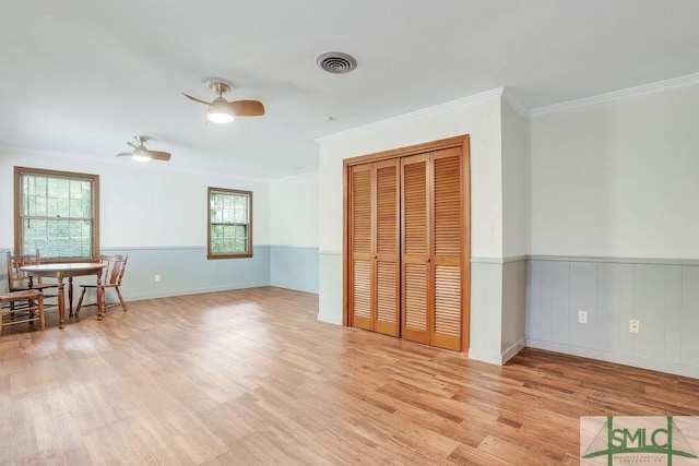 unfurnished living room with crown molding, ceiling fan, wainscoting, light wood-style floors, and visible vents