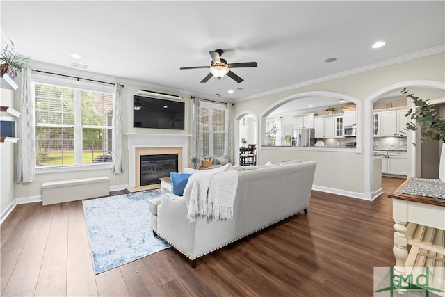 living room featuring a fireplace with flush hearth, ceiling fan, dark wood-style floors, and ornamental molding