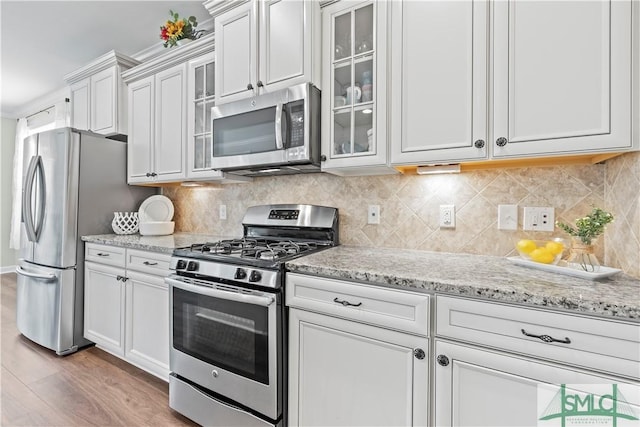 kitchen with light wood-type flooring, appliances with stainless steel finishes, light stone countertops, and glass insert cabinets