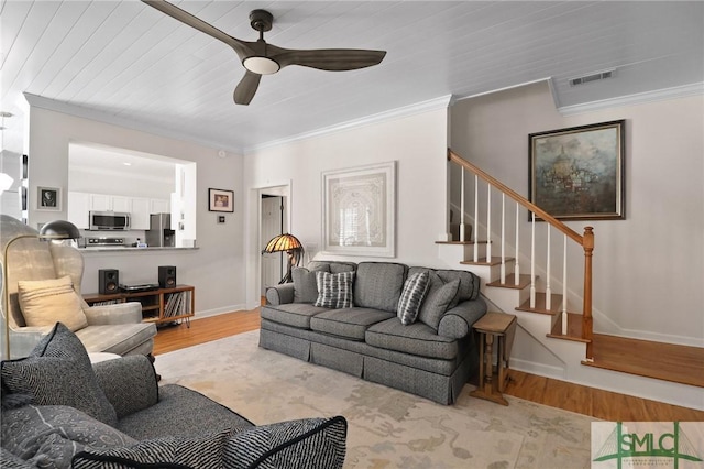 living area with ceiling fan, wood finished floors, visible vents, ornamental molding, and stairway