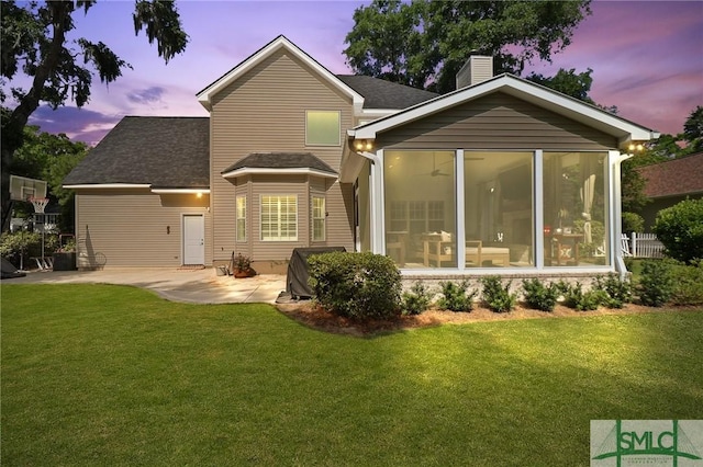 back of house at dusk with a lawn, a chimney, a sunroom, and a patio area