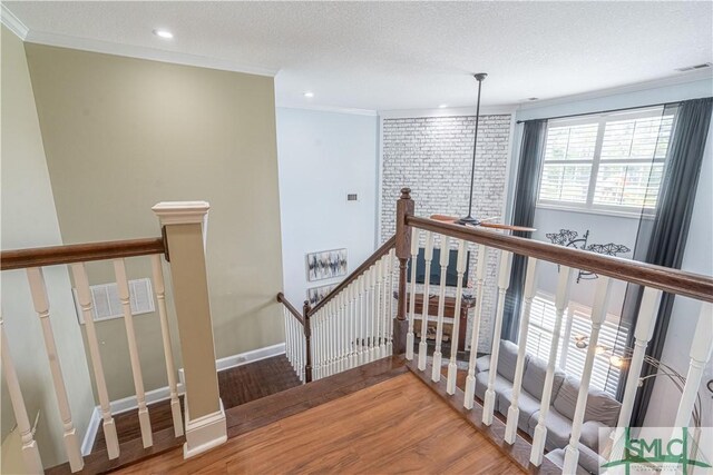 hall with crown molding, visible vents, wood finished floors, and an upstairs landing