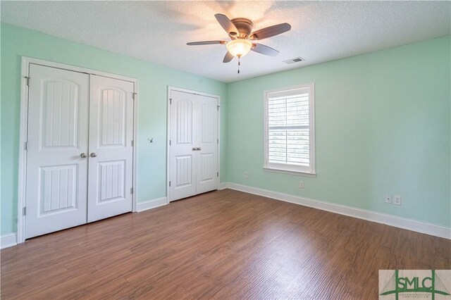 unfurnished bedroom featuring multiple closets, baseboards, wood finished floors, and visible vents