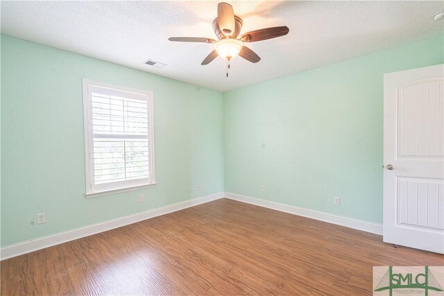 empty room with baseboards, a ceiling fan, wood finished floors, and visible vents