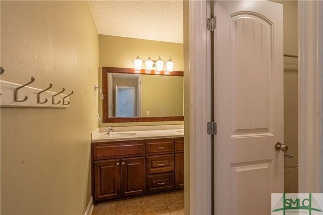 full bathroom featuring double vanity, tile patterned floors, a sink, and a textured ceiling
