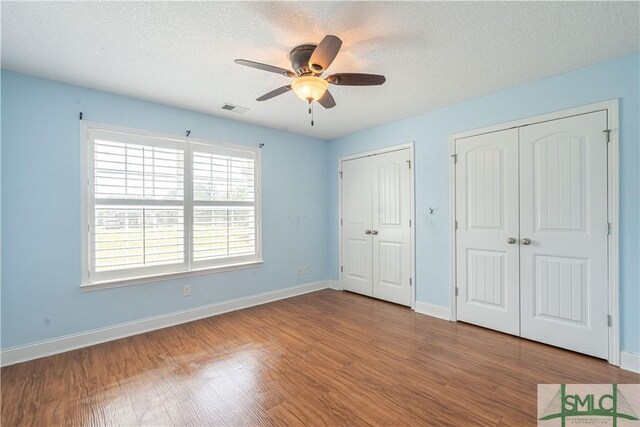 unfurnished bedroom with multiple closets, baseboards, wood finished floors, and visible vents