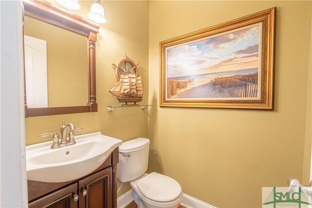 half bathroom with toilet, baseboards, and vanity