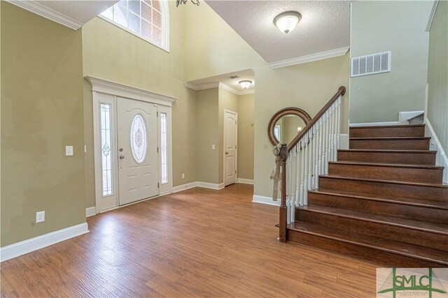 entryway featuring visible vents, crown molding, wood finished floors, stairway, and baseboards