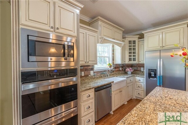 kitchen featuring cream cabinets, crown molding, appliances with stainless steel finishes, a sink, and light wood-style flooring