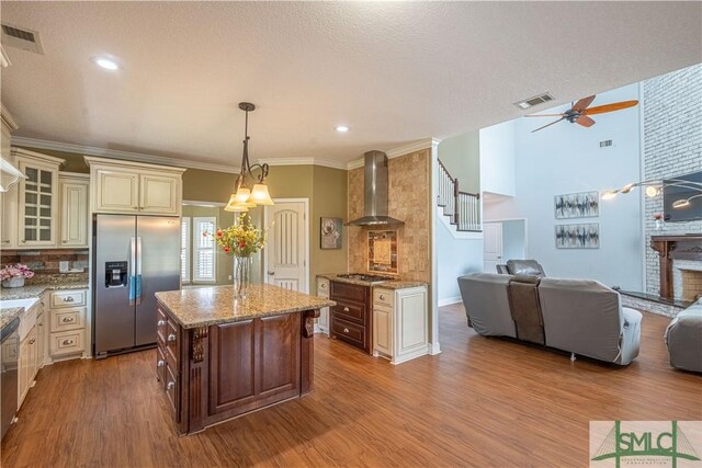 kitchen with appliances with stainless steel finishes, wall chimney exhaust hood, open floor plan, cream cabinetry, and glass insert cabinets