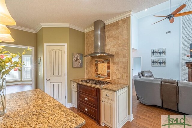 kitchen with wall chimney range hood, ceiling fan, light wood-style floors, open floor plan, and stainless steel gas stovetop