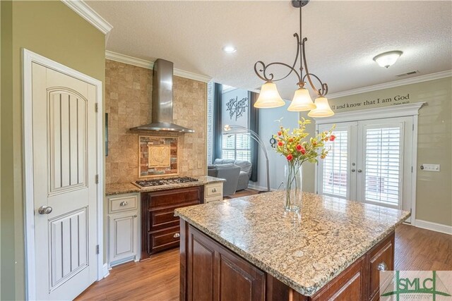 kitchen featuring wall chimney range hood, french doors, a textured ceiling, visible vents, and light wood-style flooring