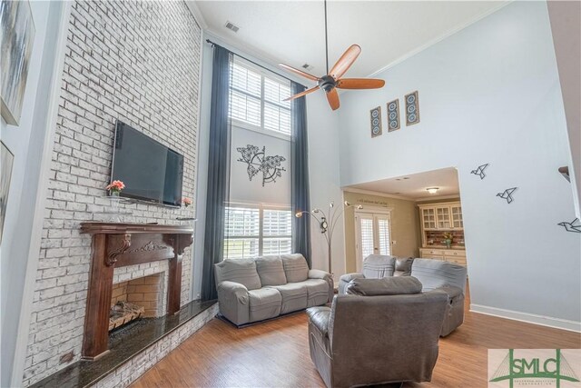living area featuring a ceiling fan, a brick fireplace, wood finished floors, and a wealth of natural light