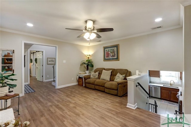 living area featuring visible vents, ornamental molding, light wood-style floors, baseboards, and a ceiling fan