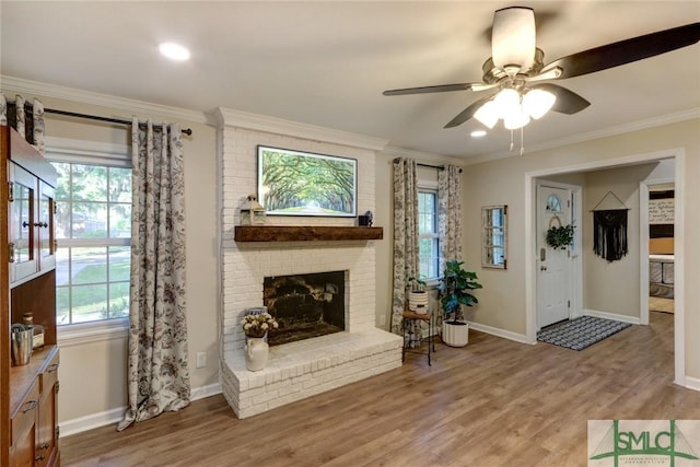 living room featuring ceiling fan, crown molding, a brick fireplace, baseboards, and light wood-style floors