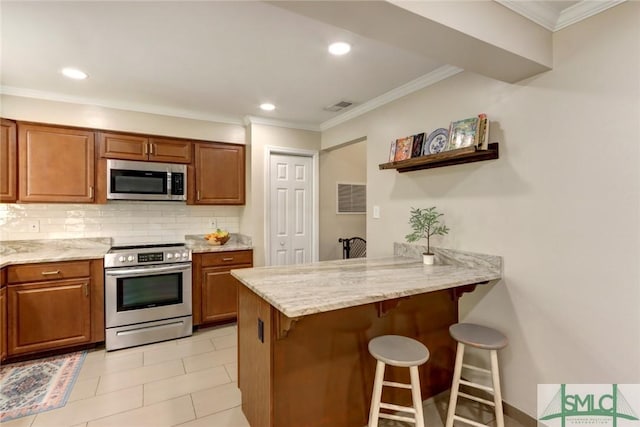 kitchen with a breakfast bar area, brown cabinets, appliances with stainless steel finishes, and visible vents