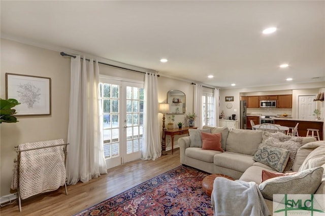 living room featuring french doors, ornamental molding, light wood-style flooring, and recessed lighting