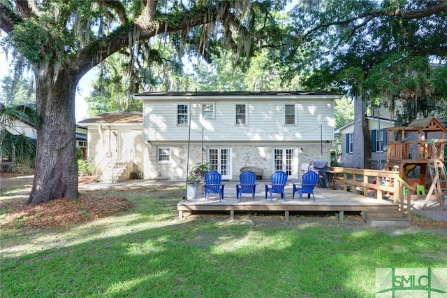 back of house with a deck, stone siding, french doors, a playground, and a yard