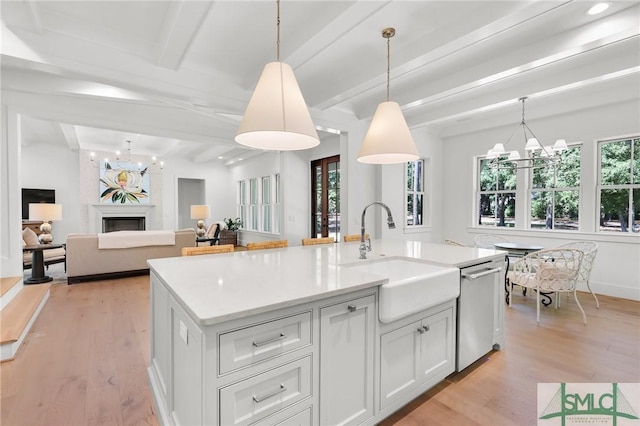 kitchen featuring an inviting chandelier, a sink, light wood-style floors, a kitchen island with sink, and stainless steel dishwasher