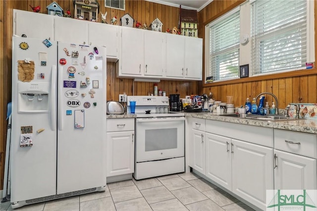 kitchen featuring visible vents, wood walls, a sink, white cabinets, and white appliances