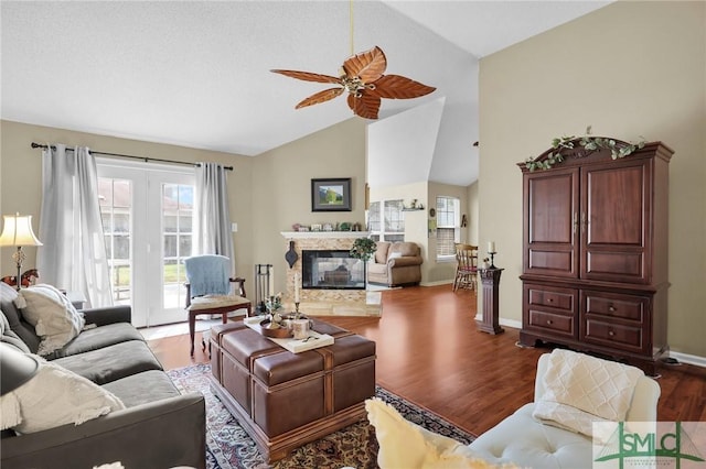 living room featuring wood finished floors, lofted ceiling, a fireplace, baseboards, and a ceiling fan