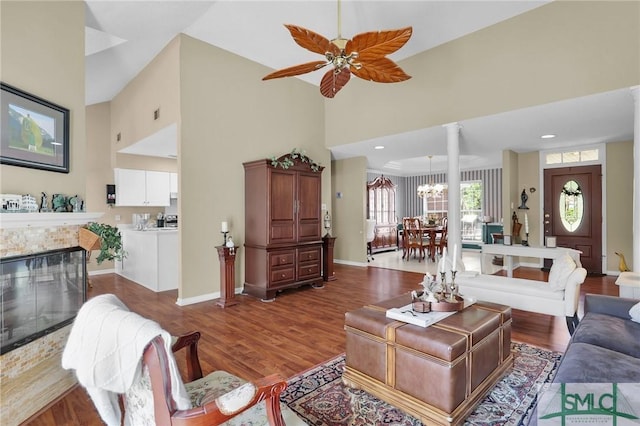 living room featuring high vaulted ceiling, a fireplace, ceiling fan with notable chandelier, and wood finished floors
