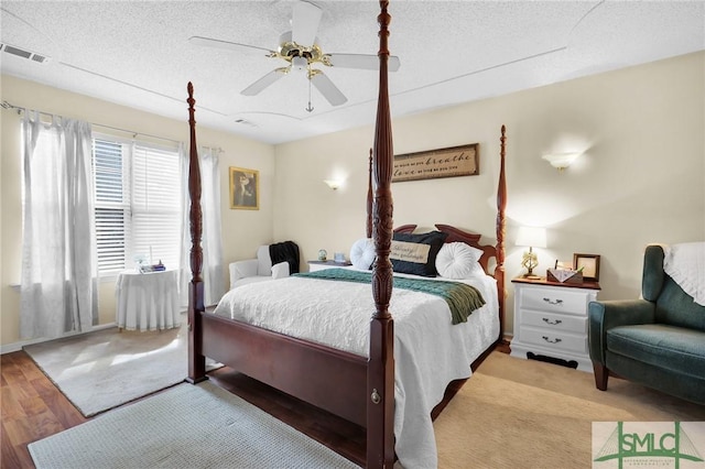 bedroom with a textured ceiling, a ceiling fan, wood finished floors, and visible vents