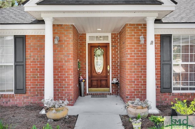 entrance to property with roof with shingles and brick siding