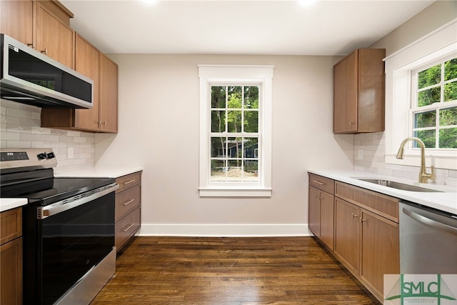 kitchen with baseboards, dark wood-type flooring, a sink, appliances with stainless steel finishes, and backsplash