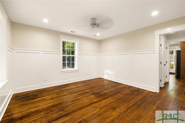 spare room with a ceiling fan, a decorative wall, dark wood-style floors, and a wainscoted wall