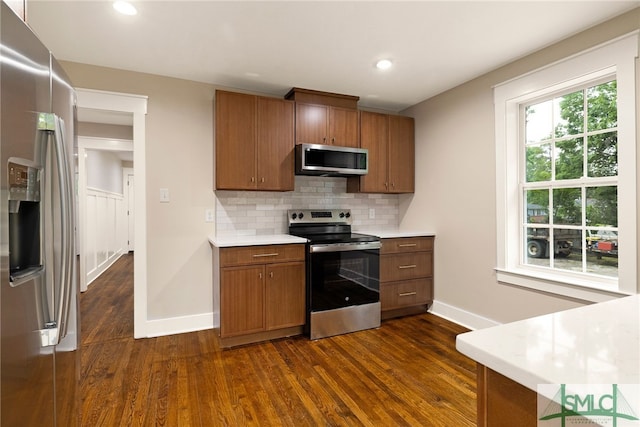 kitchen with brown cabinetry, light countertops, dark wood finished floors, appliances with stainless steel finishes, and backsplash