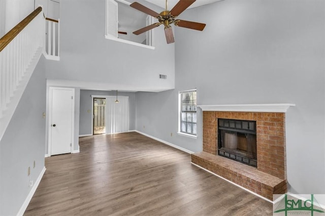 unfurnished living room with a fireplace, a ceiling fan, wood finished floors, and a towering ceiling