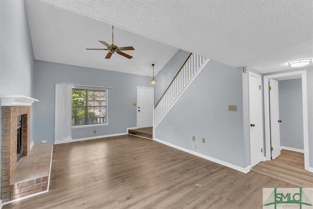 unfurnished living room with wood finished floors, a fireplace, stairway, a textured ceiling, and a ceiling fan