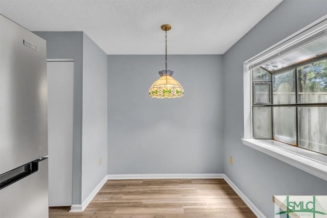 unfurnished dining area featuring a textured ceiling, baseboards, and wood finished floors