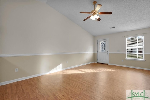 empty room featuring ceiling fan, vaulted ceiling, light wood-style flooring, and visible vents