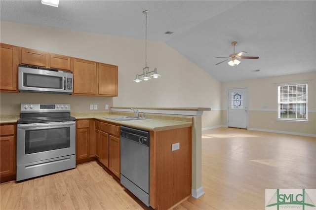 kitchen featuring appliances with stainless steel finishes, a sink, a peninsula, lofted ceiling, and light wood-style floors