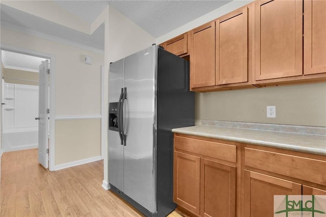 kitchen with crown molding, stainless steel fridge, light countertops, a textured ceiling, and light wood-type flooring