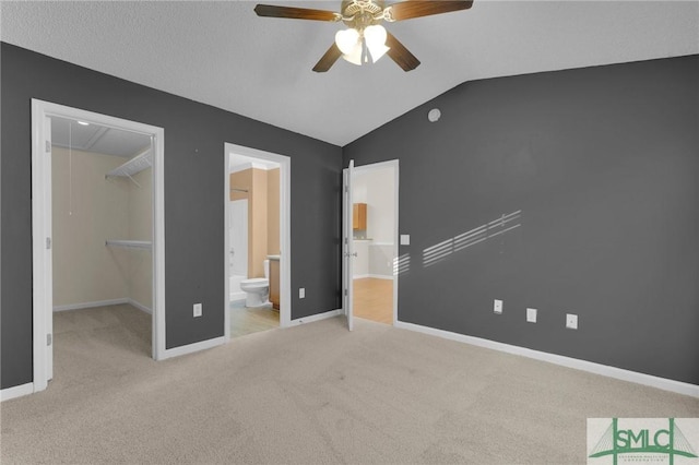 unfurnished bedroom featuring a walk in closet, carpet floors, a closet, lofted ceiling, and ensuite bath