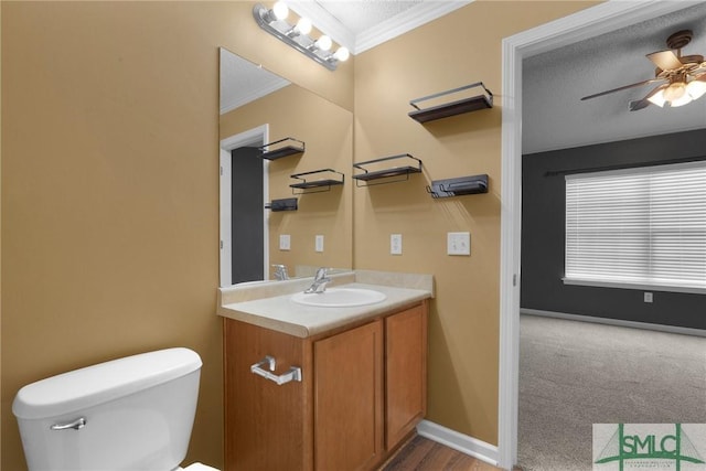 bathroom with ceiling fan, crown molding, vanity, baseboards, and toilet