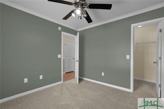 unfurnished bedroom featuring crown molding, baseboards, a textured ceiling, a spacious closet, and carpet flooring